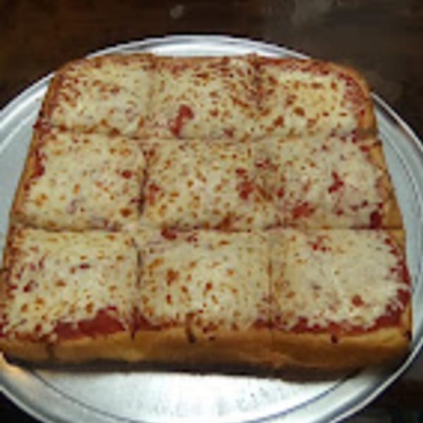 A rectangular Brooklyn Pizza cheese pizza, cut into nine squares, on a metal pizza pan.