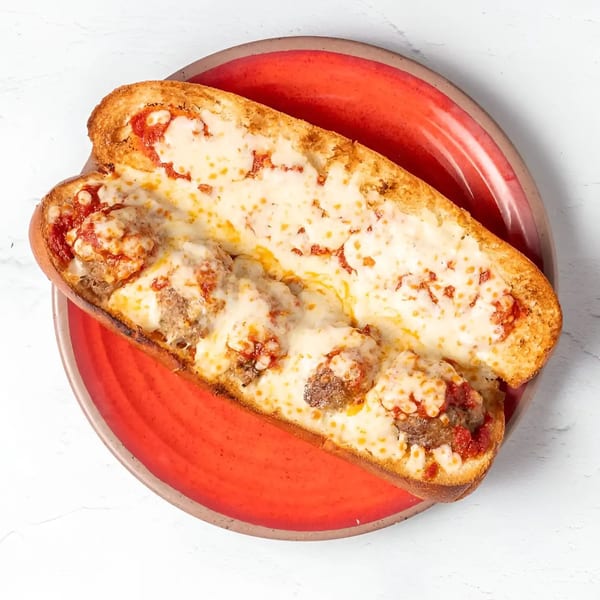 A meatball sub with melted cheese and marinara sauce on a red plate.