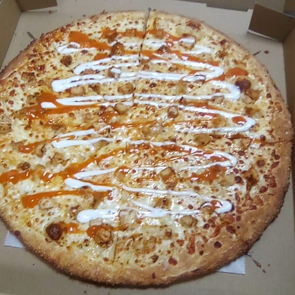 A Brooklyn Pizza buffalo chicken pizza, drizzled with white and orange sauces, in a cardboard box.