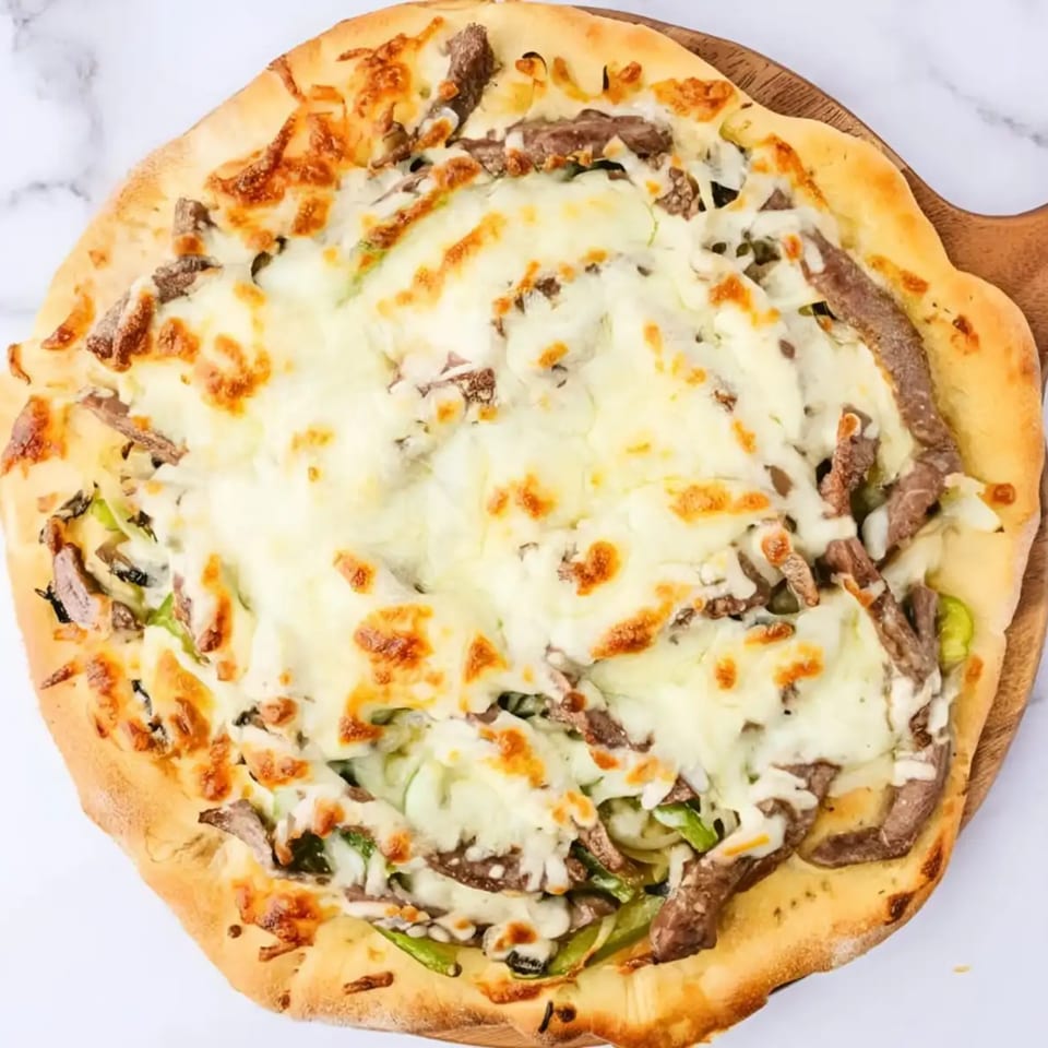 Cheesesteak pizza with melted mozzarella, sliced steak, and green peppers on a wooden peel.