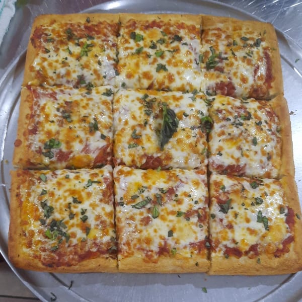A square Brooklyn Pizza, cut into nine slices, with melted cheese, tomato sauce, and basil.
