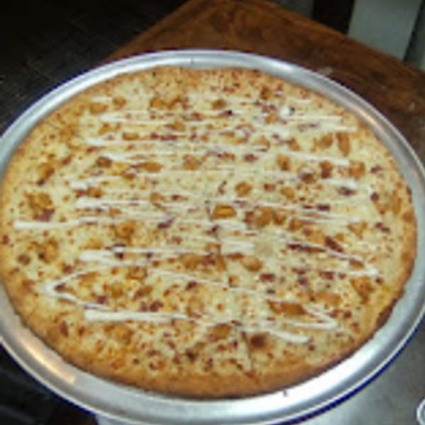 A whole Brooklyn Pizza chicken bacon ranch pizza, drizzled with white sauce, on a metal pan.