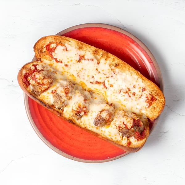 A Brooklyn Pizza meatball sub, topped with melted cheese and marinara sauce, on a red plate.