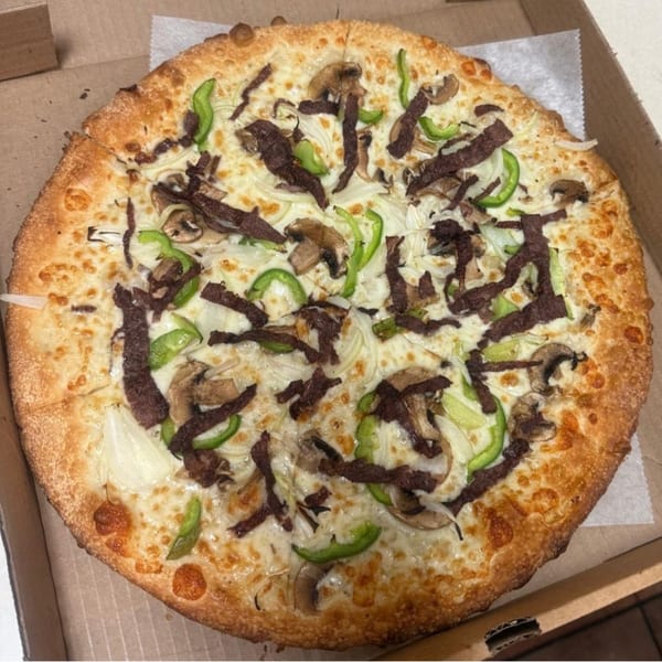 A Brooklyn Pizza cheesesteak pizza with white cheese, steak, green peppers, onions, and mushrooms.
